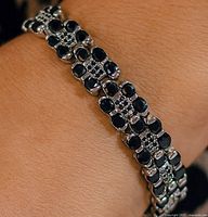 Bracelet worn on wrist showing overall design with dark sapphires in silver setting