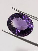 Front view of oval faceted amethyst held by tweezers