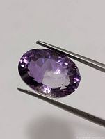 Front view of oval faceted purple amethyst held by tweezers