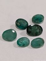 Six green oval faceted emeralds on white background