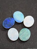 Five oval opal cabochons showing varied blue, green and white coloration