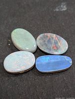 Four loose oval opal cabochons on dark background