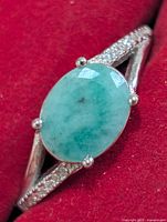 Front view of ring showing oval green stone and split shank with clear accents