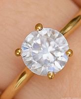 Close-up of ring on finger showing round moissanite and four-prong setting