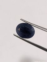 Front view of oval faceted sapphire held by tweezers