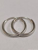 Pair of silver hoop earrings lying overlapping, front view displays polished surface and circular shape