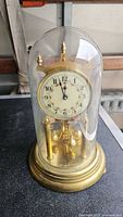 Front view of brass anniversary clock under glass dome