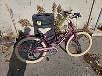 Left side view of purple step-through cruiser bicycle leaning against tires