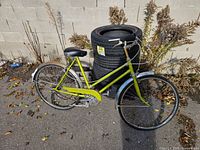 Left side profile of lime green step-through bicycle leaning against stacked tires