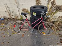 Left side view of entire red road bicycle leaning against stack of tires