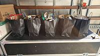 Five paper tote bags lined up, each filled with loose LEGO pieces
