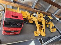 Front view showing red dump truck cab, detached yellow bed, excavator and loader