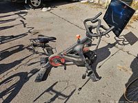 Left side profile of Peloton bike showing frame, flywheel, pedals, handlebars and touchscreen