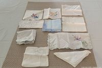 All ten handkerchiefs laid out showing variety of embroidery, lace and colours
