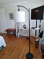 Full view of arched floor lamp in room showing black metal body, round base, white drum shade