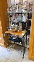 Full view of baker's rack showing metal frame, wood top, glass shelves