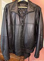 Front view of black leather bomber jacket on hanger showing full design