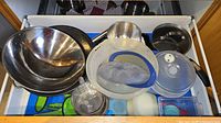 Drawer view showing stainless bowls, skillet, saucepan lid, plastic bowls and utensils