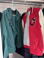 Green rainsuit jacket on hanger beside red and cream varsity jacket
