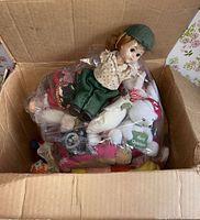 Open box showing bag of assorted plush toys and porcelain doll on top