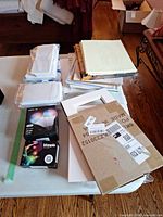 Full lot on table showing smart bulb box, ink cartridge box, stacked mats, cardstock, and cardboard sheet