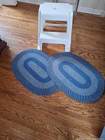 Two blue and white oval braided rugs with white plastic two-step stool upright