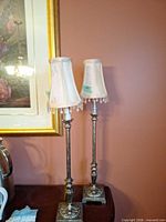 Pair of tall antique silver tone lamps with shades on table