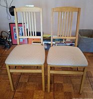 Front view of two light oak Stakmore folding chairs with beige upholstered seats