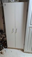 Front view of tall white laminate two-door storage cabinet with metal handles