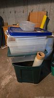 stack of clear bins with blue lid, small container on top, roll of plastic wrap in front of green tote