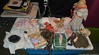 Overview of table with doll heads, bodies, limbs, wigs, clothing, basket