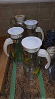Three citrus print pitchers with white lids and metal collars