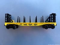 Side view of yellow Lionel 16375 flatcar with stakes