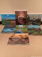 Seven acrylic landscape paintings displayed together to show entire lot