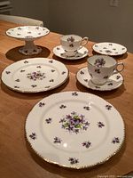 Full set displayed on table showing all eight pieces including pedestal cake stand, plates, cups, saucers