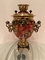 Front view of brass samovar with painted strawberry floral design, handles and spigot visible