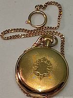 Closed gold-tone pocket watch laying flat with attached chain visible