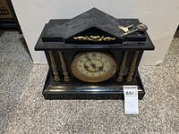 Front view of black mantel clock showing dial, columns, pediment