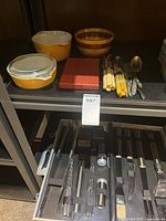 Overall lot on shelf showing Pyrex dishes with lid, wooden bowl, cutlery, red cloth and BBQ utensil case