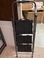 Ladder folded flat against wall showing three black steps and gray frame