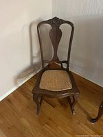 Front view of wooden rocking chair showing cane seat and carved crest