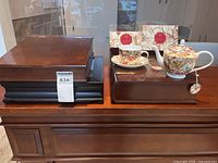 Left view showing closed flat jewelry case on black base beside other items