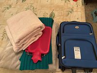 Blue suitcase closed alongside folded towels, hot water bottle, blanket, throw