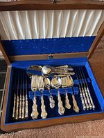 Flatware set arranged in blue-lined wood chest showing forks, spoons and serving pieces