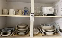 Overall view of cupboard showing casseroles, mugs, glasses, and stacks of plates and bowls