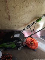 Side view of Greenworks lawn mower with rear bag and orange extension cable coiled beside it