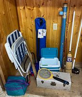 Group shot of all items leaning against wood wall: rods, chairs, cooler, toolbox, bat, broom, bug zapper, pump, soft cooler
