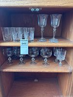 Cabinet shelves with all twelve glass pieces arranged: top shelf tumblers and goblets, lower shelf coupes