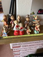Group of nine Goebel figurines on mantel with tape for scale