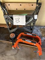 Folded Black & Decker Workmate frame, two orange Workhorse brackets, loose wheel